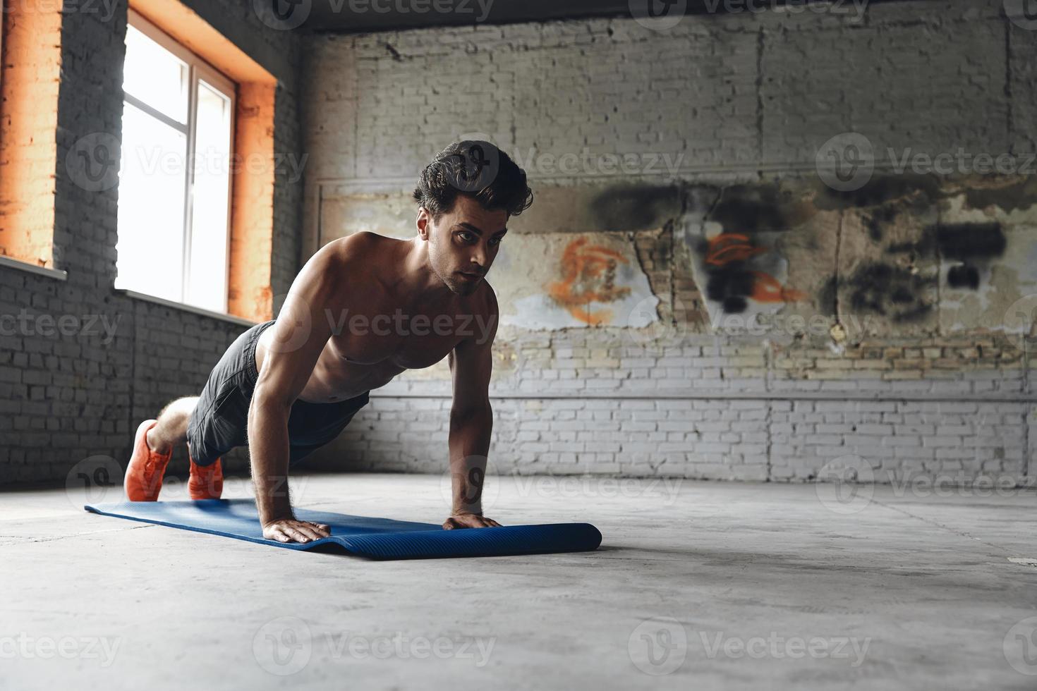 Confident young man doing push-up exercises in gym photo