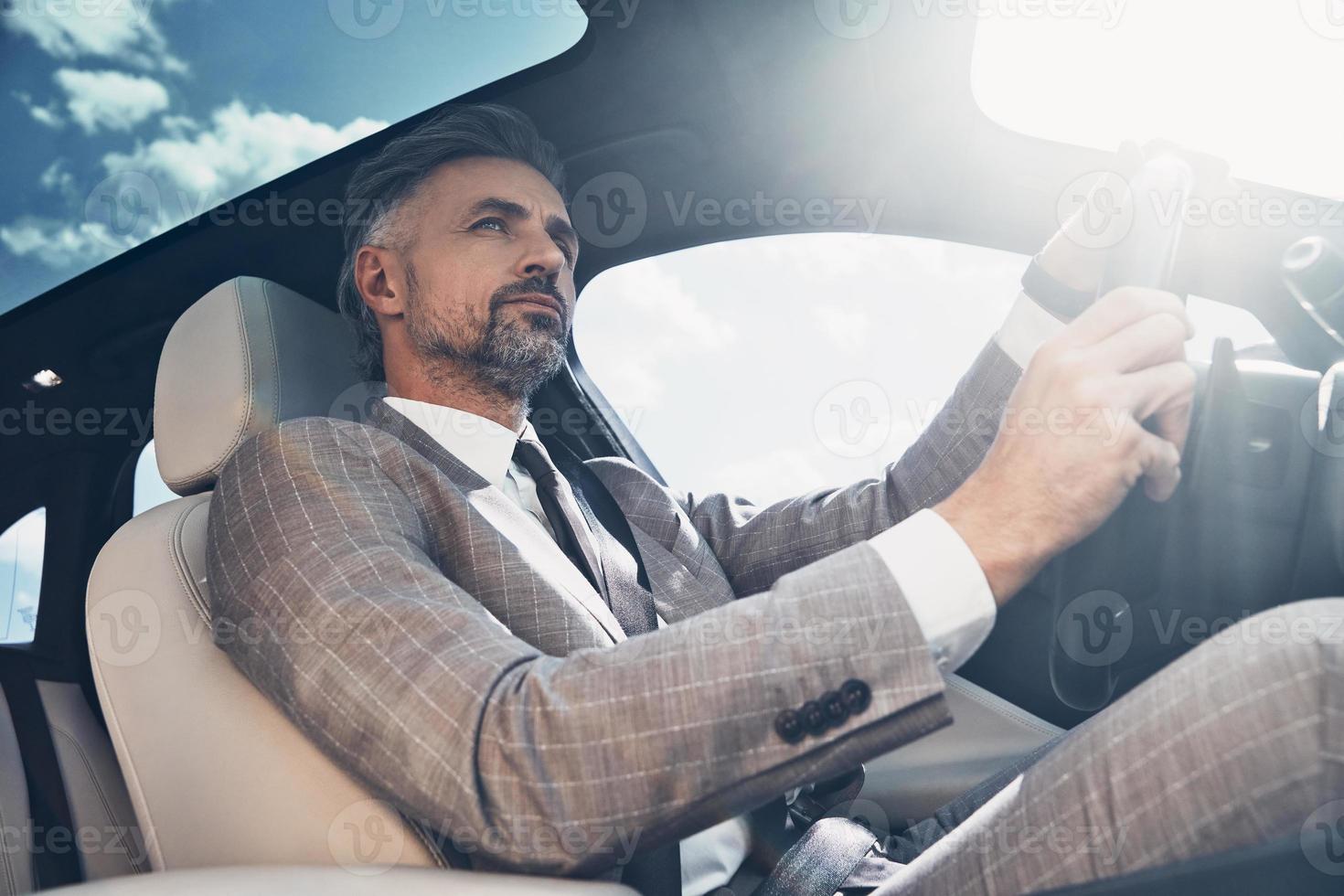 vista de ángulo bajo del hombre maduro guapo en ropa formal conduciendo un coche foto