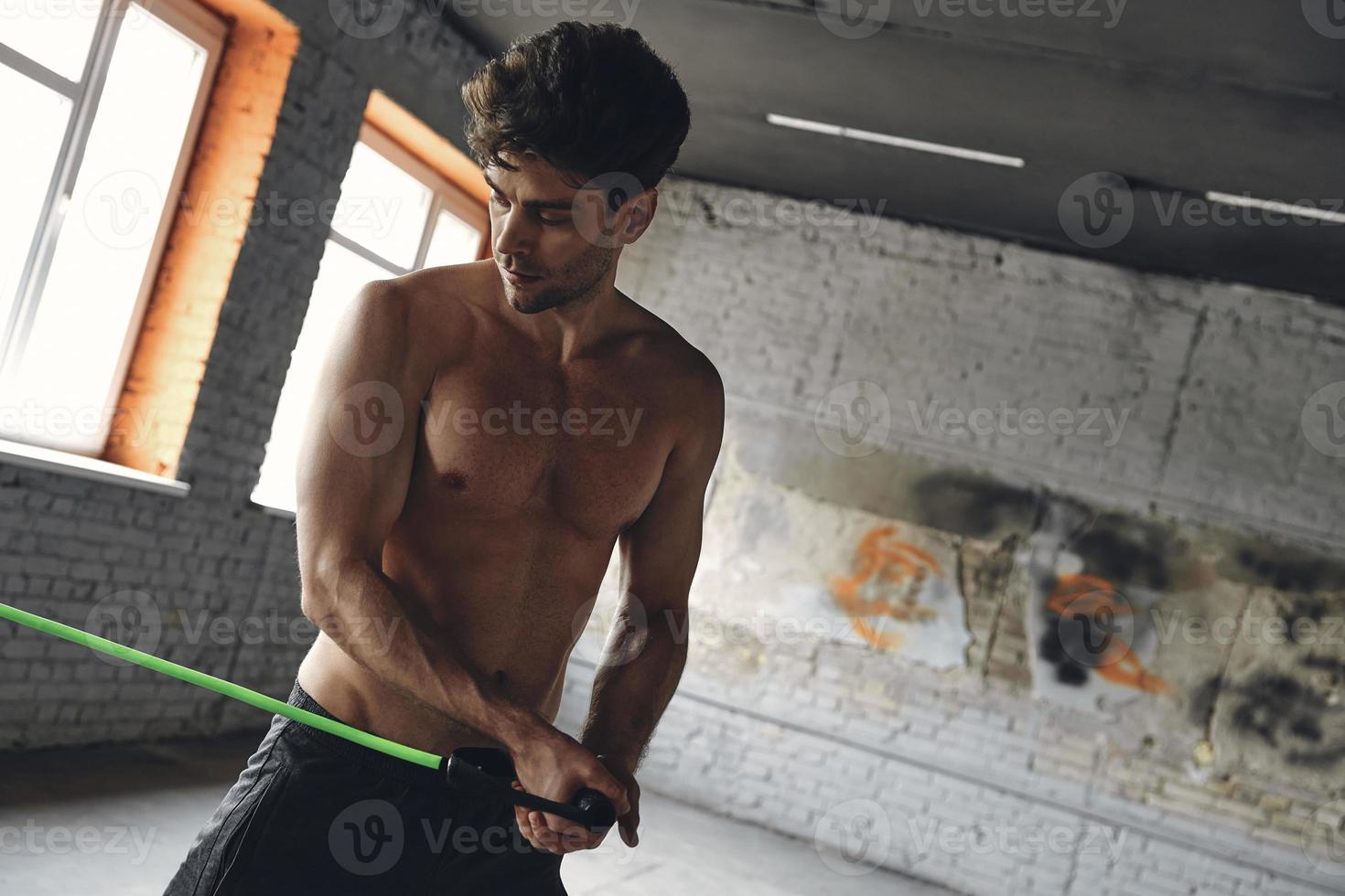 Handsome young man exercising with elastic resistance band in gym photo