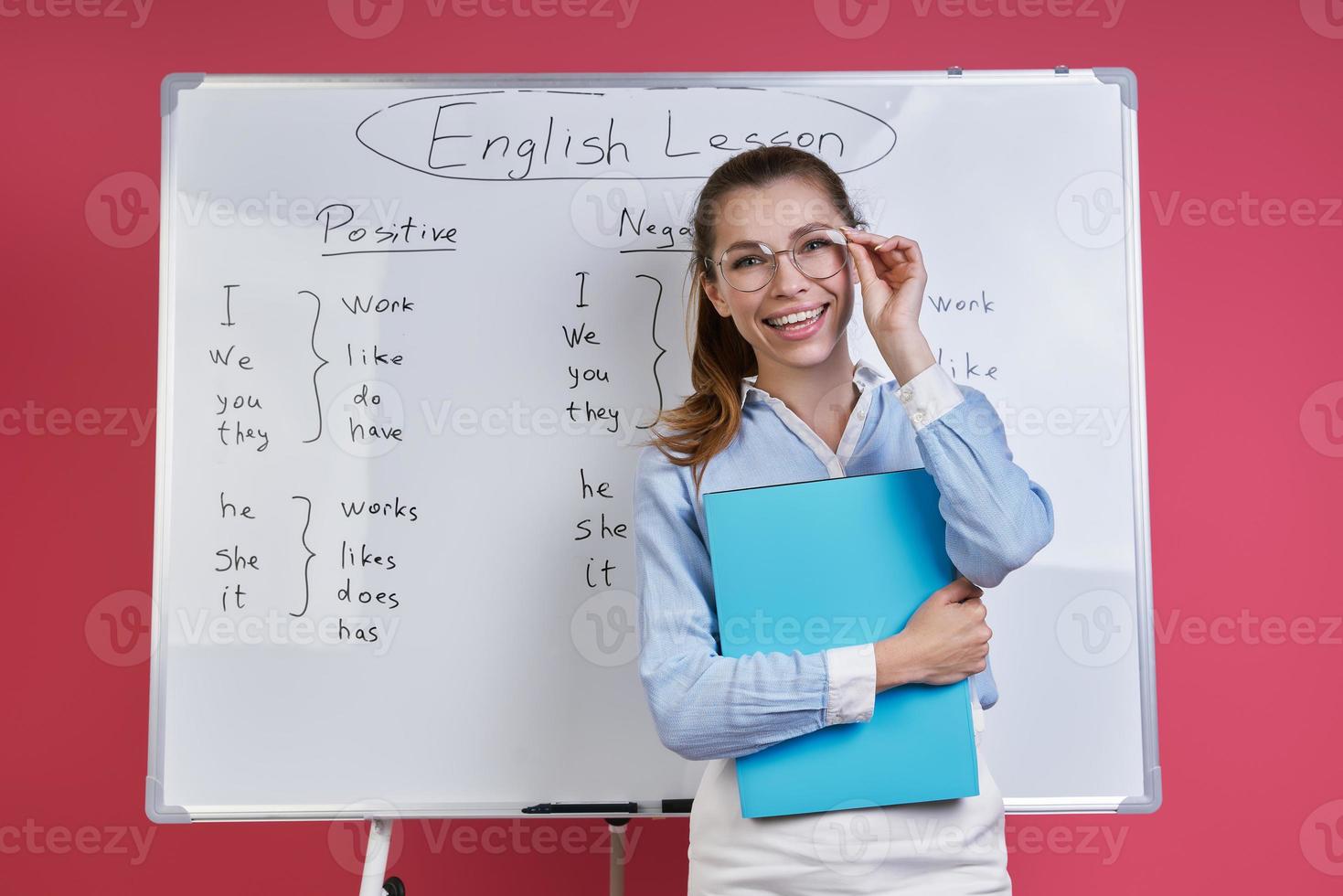 Confident young woman adjusting eyeglasses and smiling near the whiteboard against pink background photo