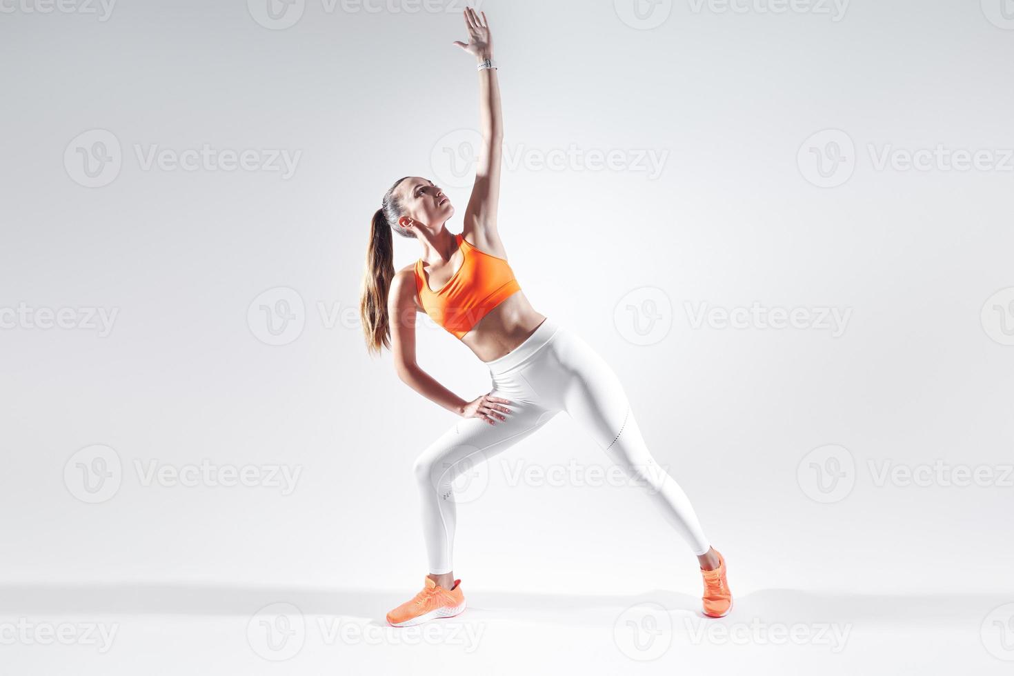 Beautiful young woman in sports clothing doing stretching exercises against white background photo