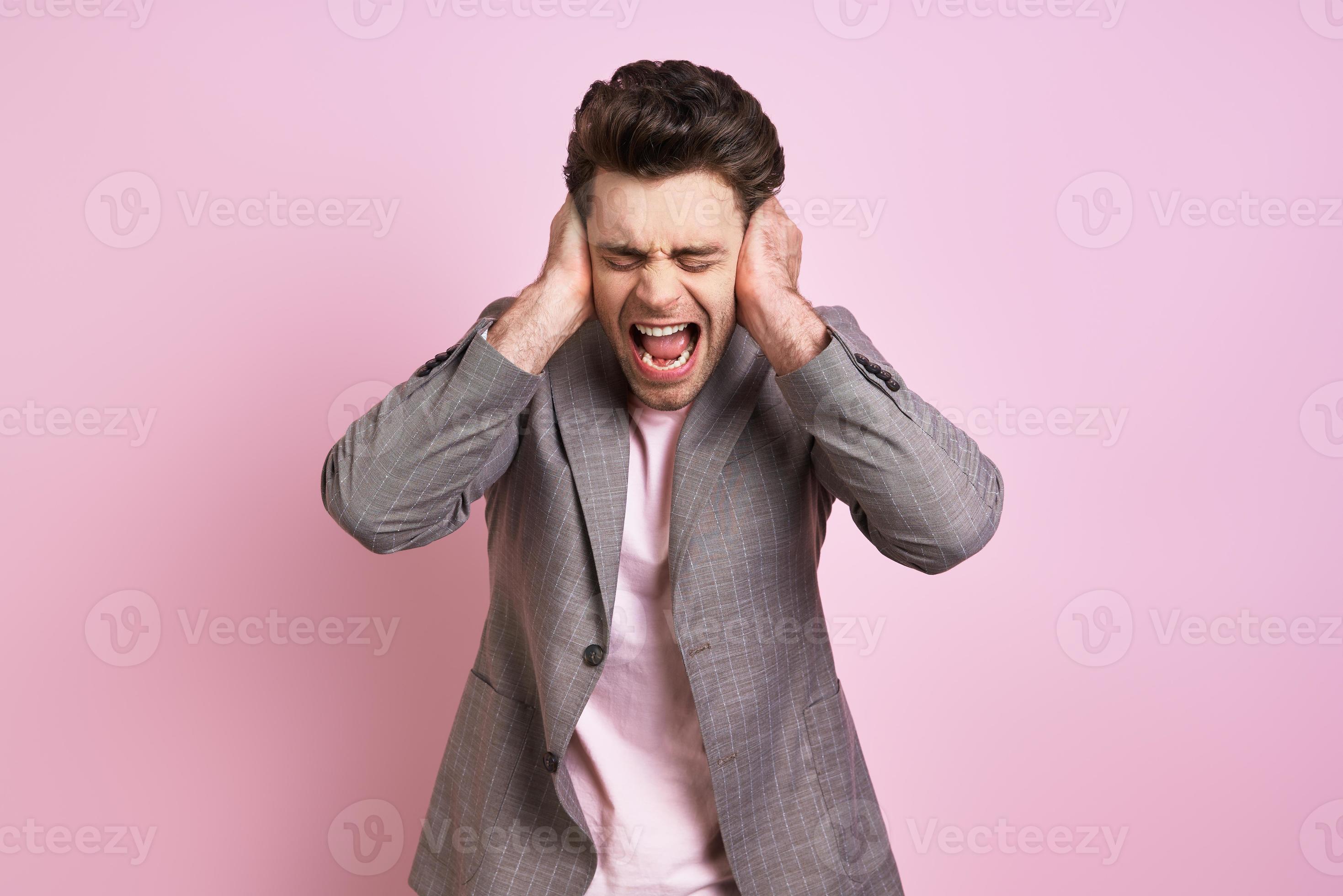 Frustrated man covering ears with hands and shouting while standing
