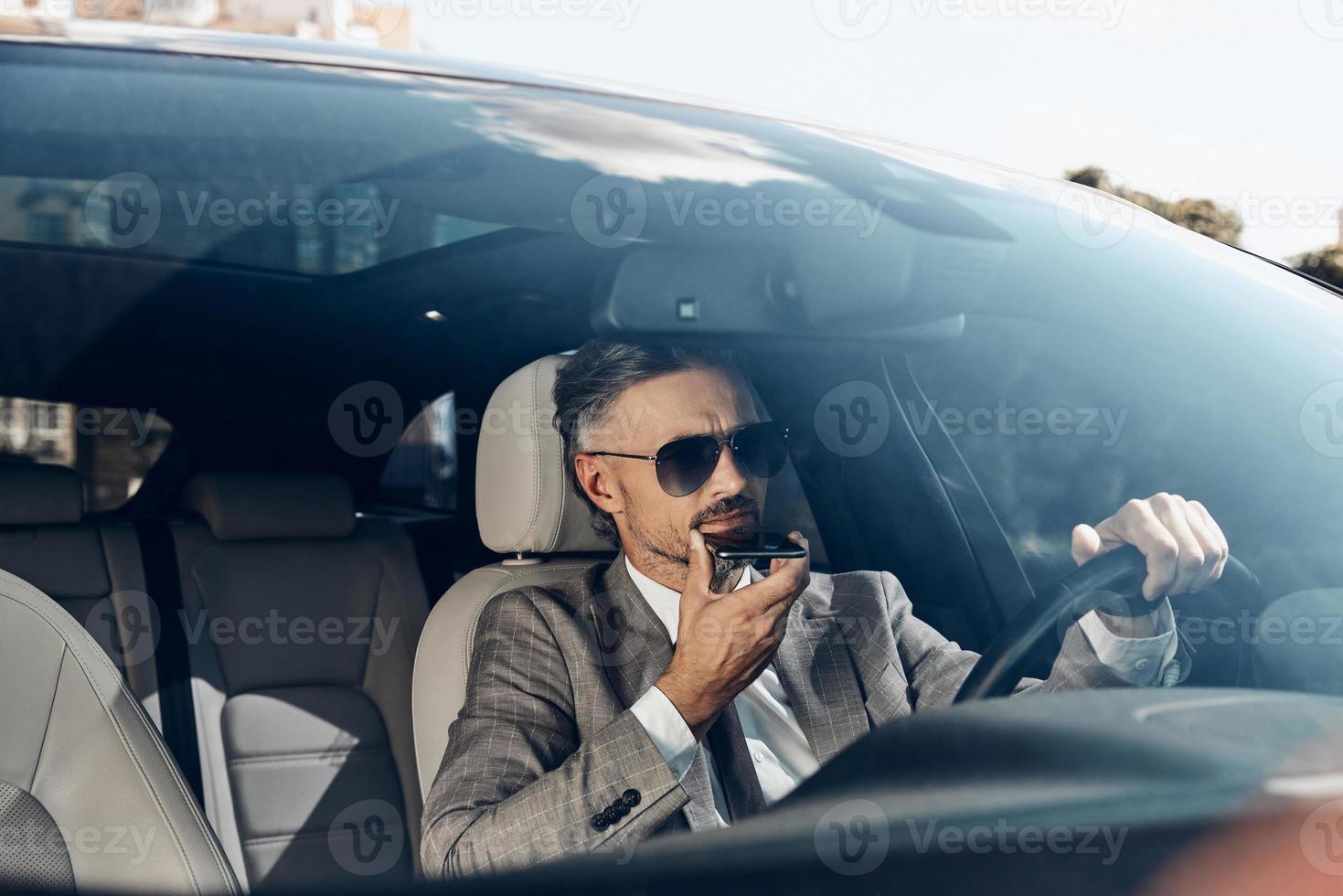 Confident man in formalwear using loudspeaker while talking on mobile phone from car photo