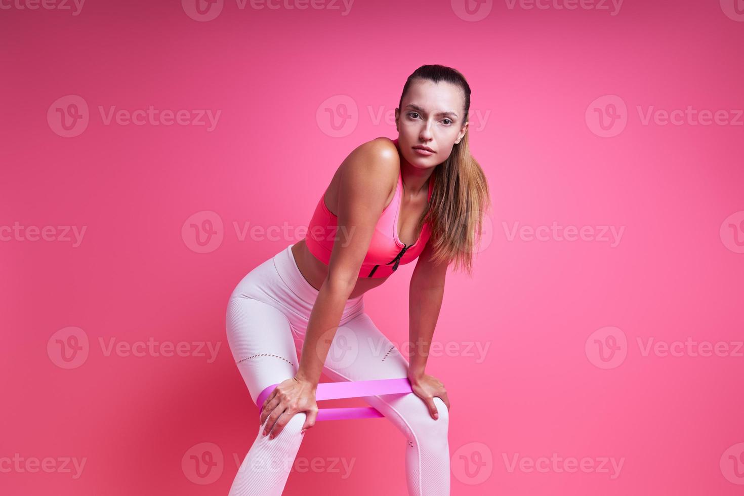 Beautiful young woman exercising with elastic band against pink background photo