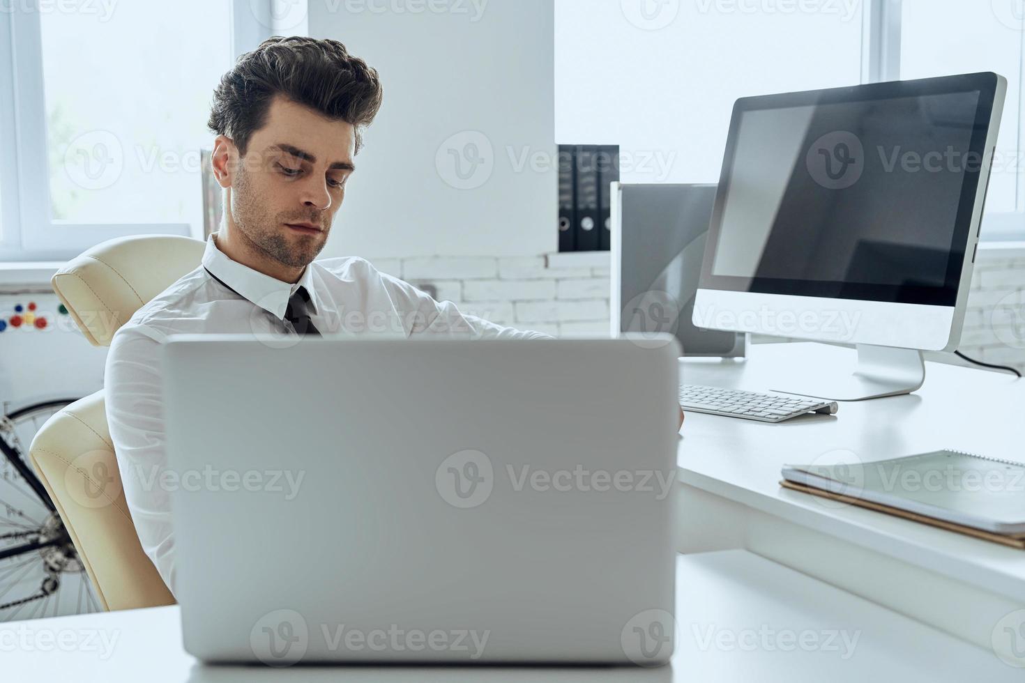 Handsome young man using computer while sitting at his working place in office photo