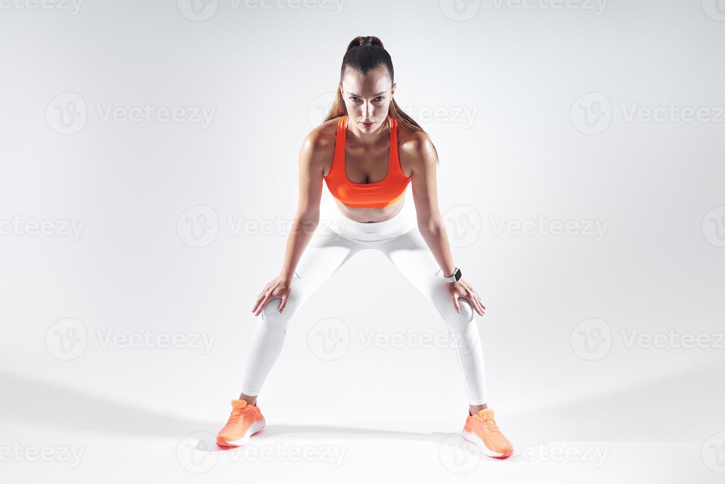 Beautiful young woman leaning on knees while standing against white background photo