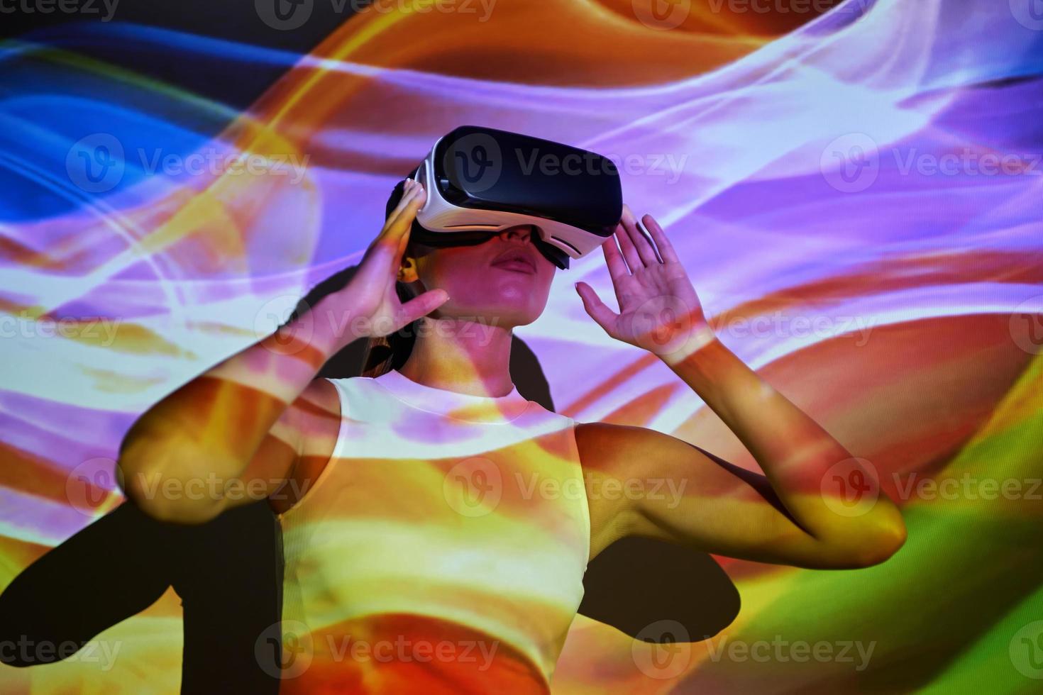 Confident young woman adjusting her virtual reality glasses against colorful background photo