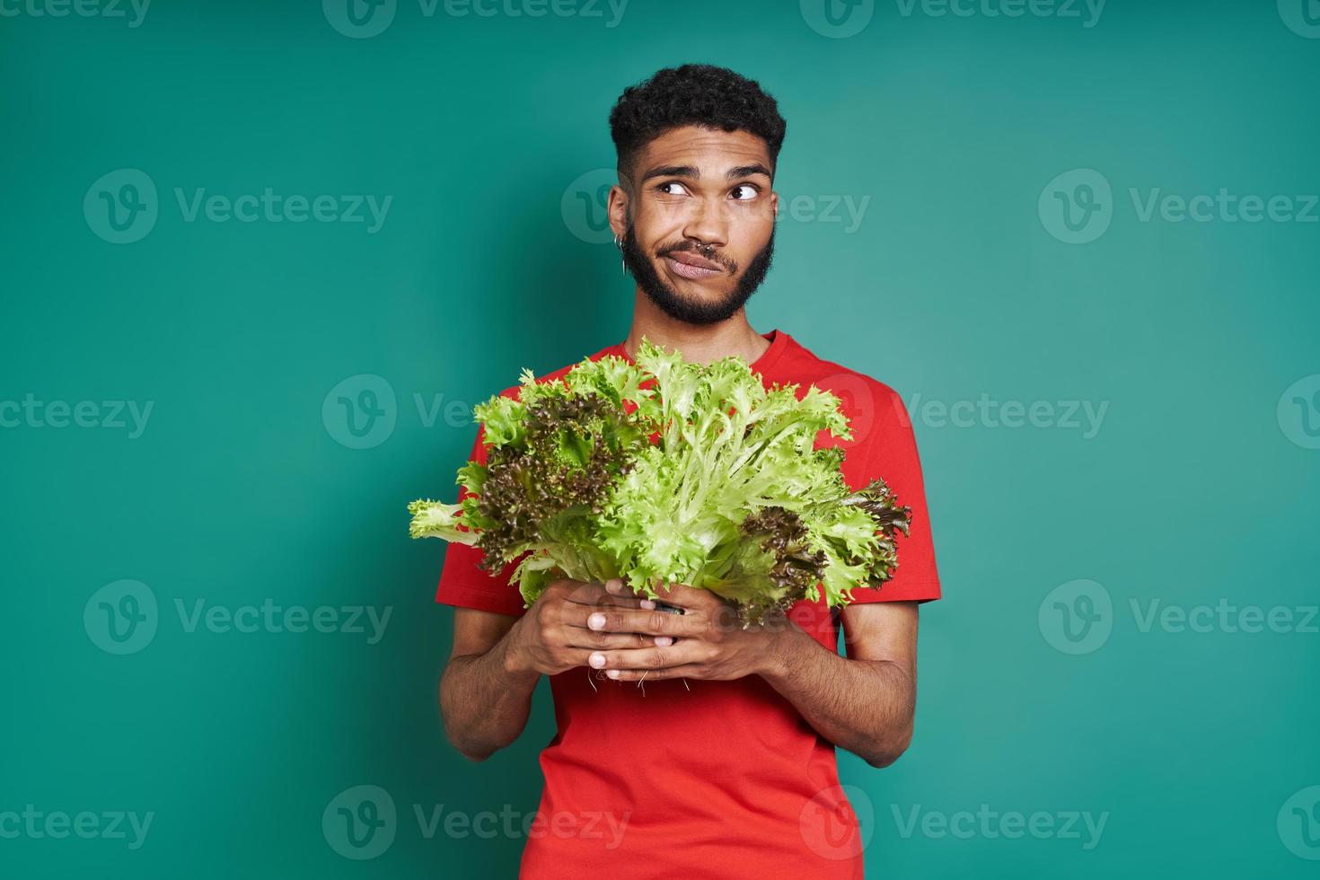 Young African man looking frustrated while holding a bunch of lettuce against green background photo