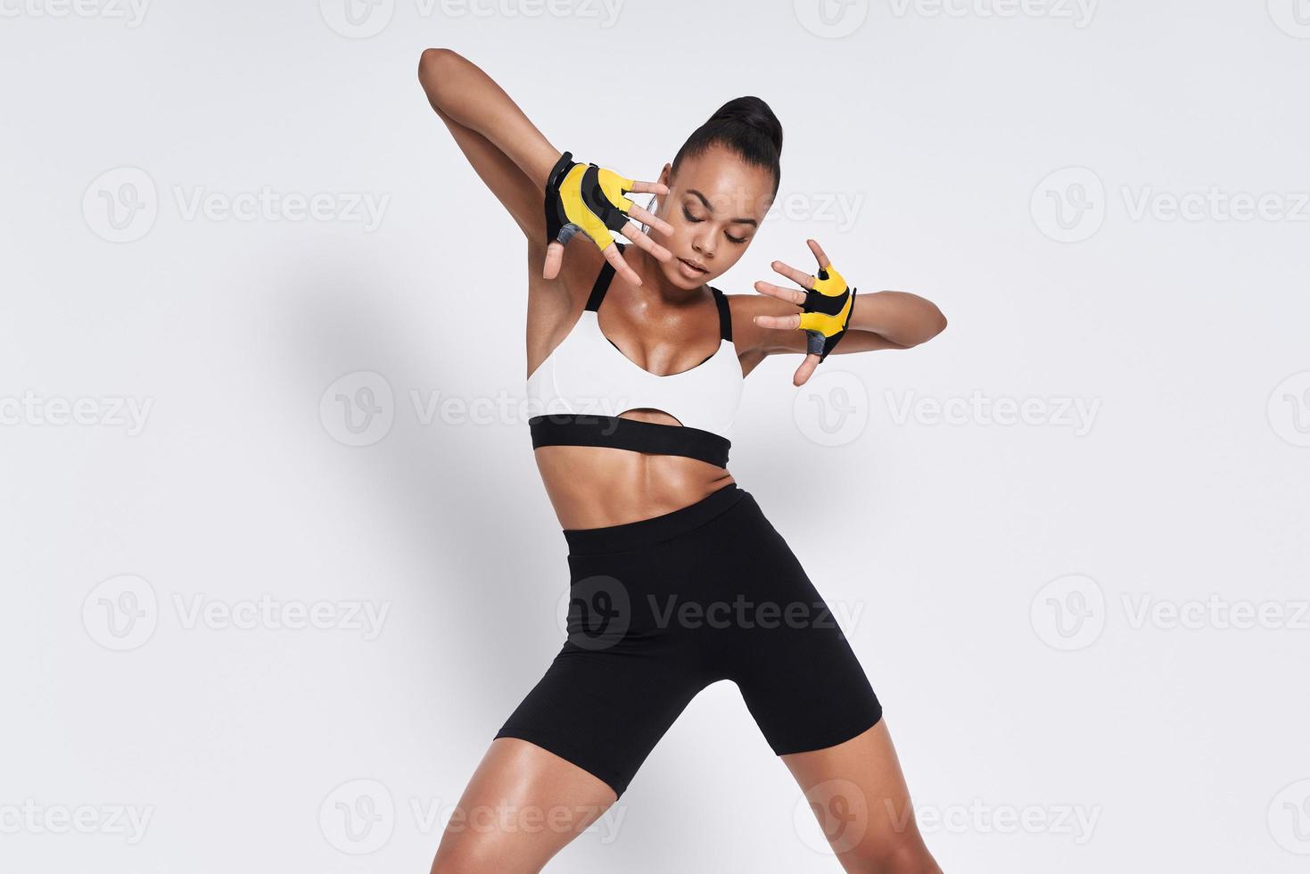 Beautiful young African woman in sports clothing dancing against white background photo