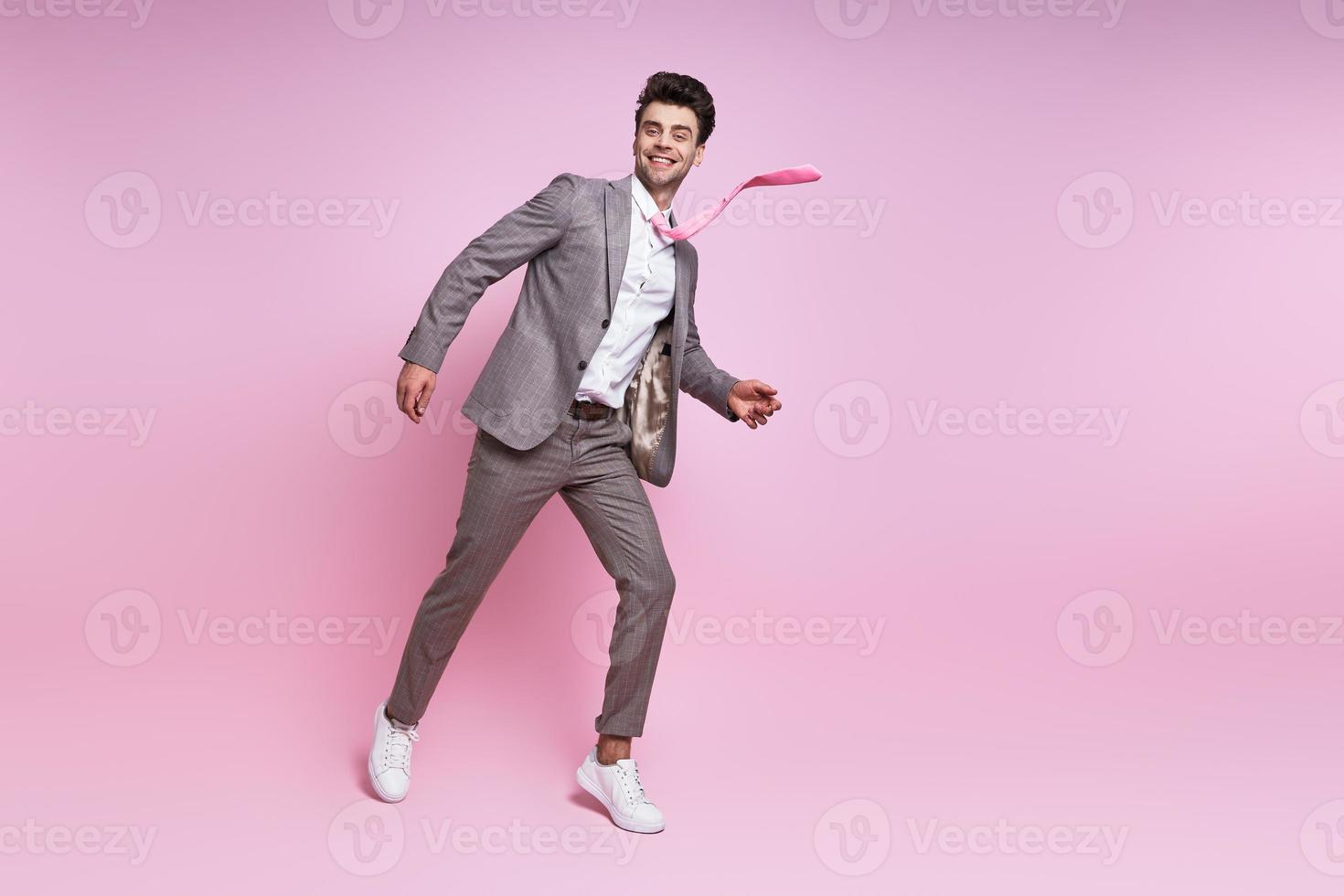 Excited young man in full suit smiling while moving against pink background photo