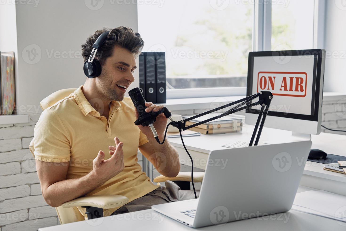 apuesto joven usando micrófono y gesticulando mientras graba podcast en el estudio foto