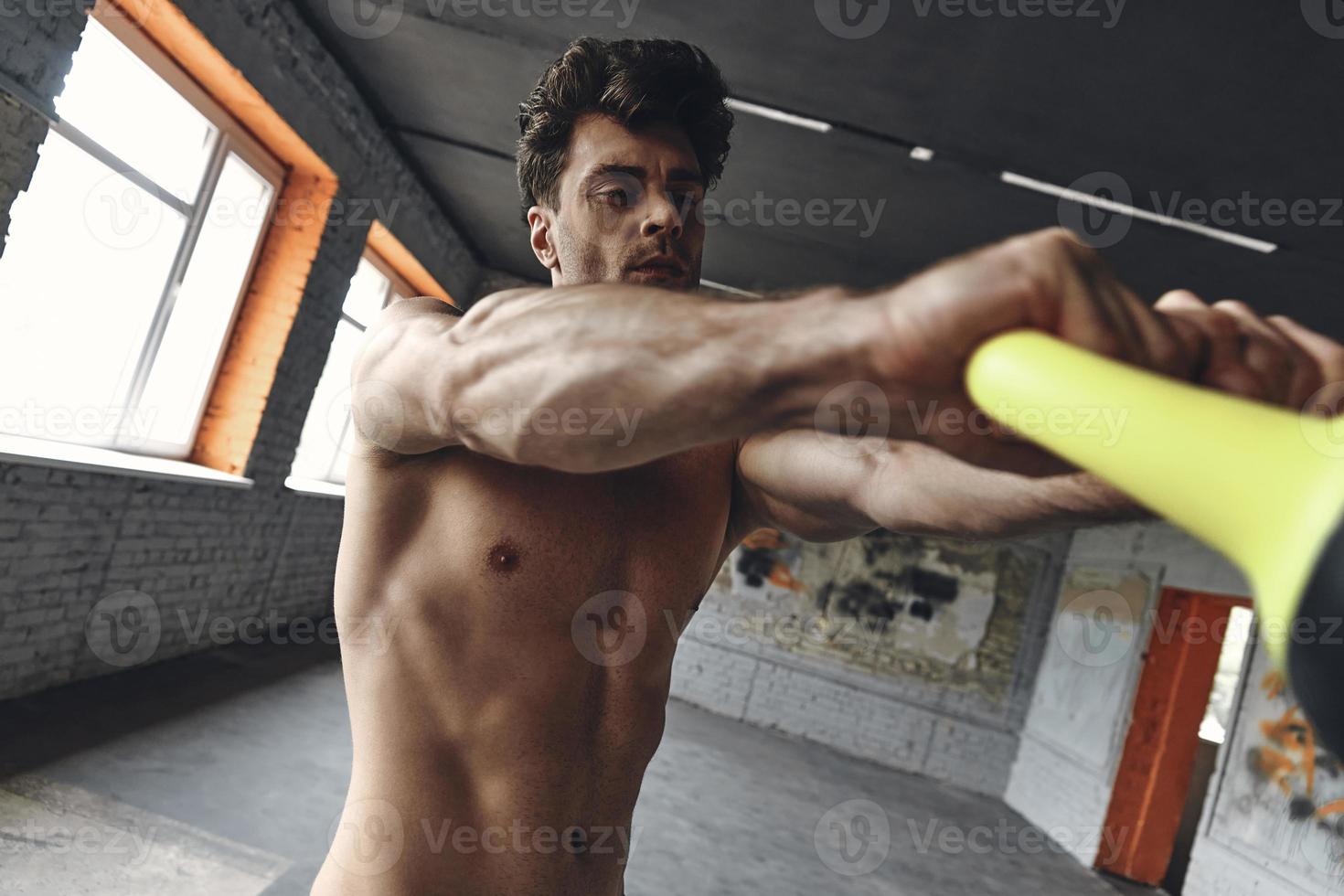 Young muscular man exercising with kettlebell while standing in gym photo