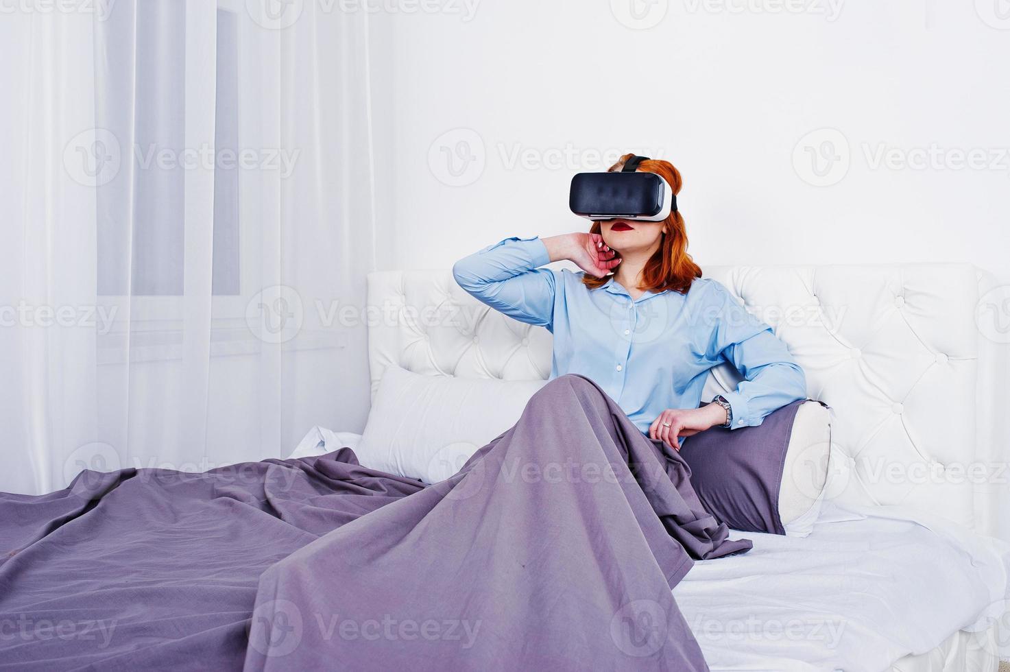 Red haired girl in bed with vr glasses at studio room. photo