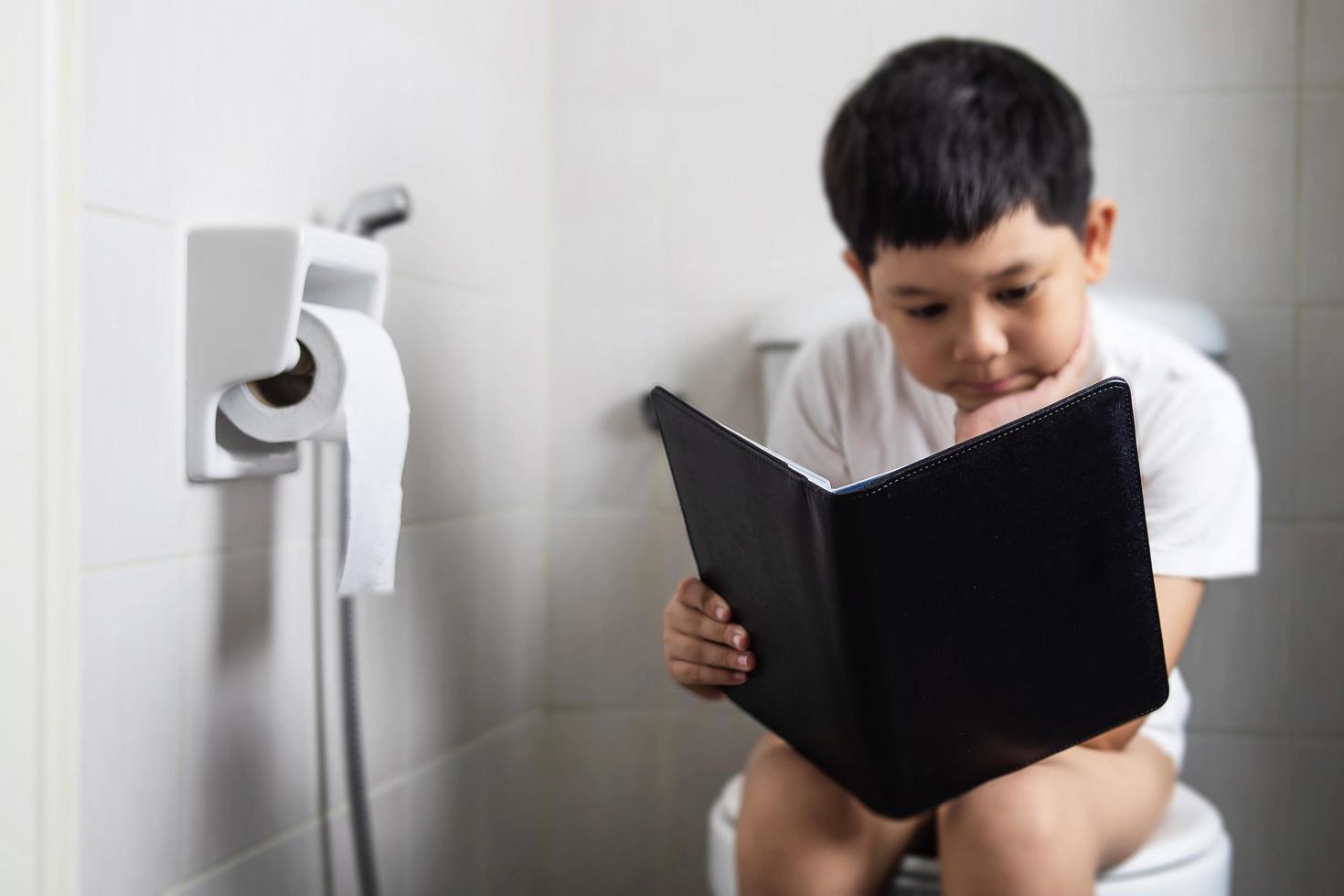 Asian boy sitting on toilet bowl while reading book - health problem concept photo