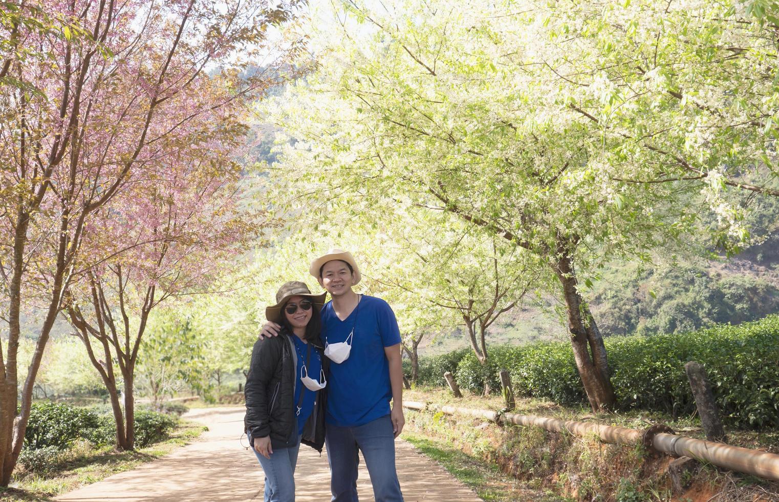 pareja asiática feliz tomando fotos en la hermosa naturaleza prunus cerasoides sakura del jardín de flores de tailandia en doi ang khang, chiangmai tailandia