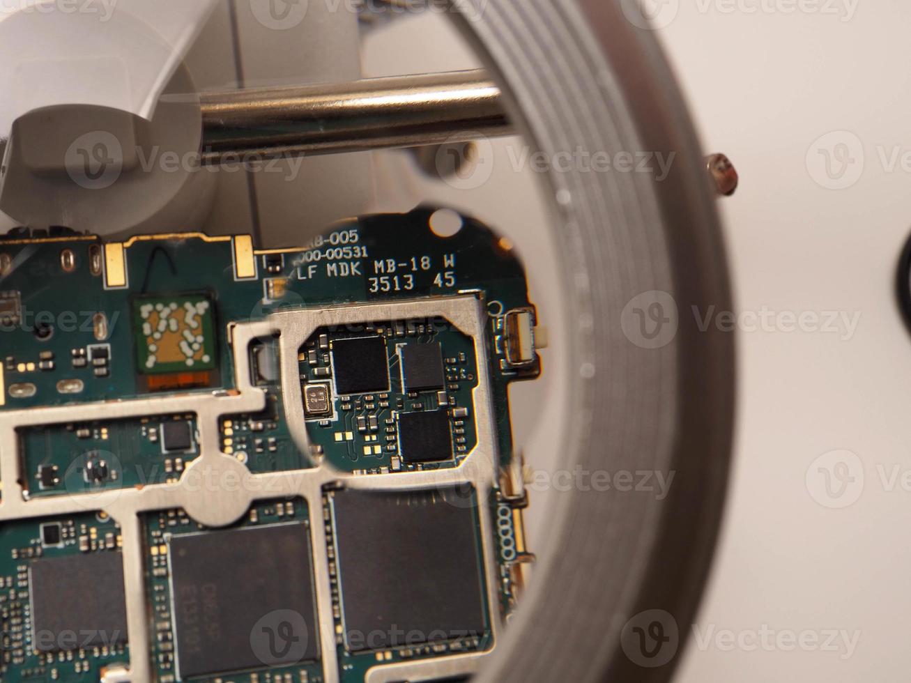 Close up shoot of printed circuit board PCB sitting on a white repair stand with magnifier for better examining small parts photo