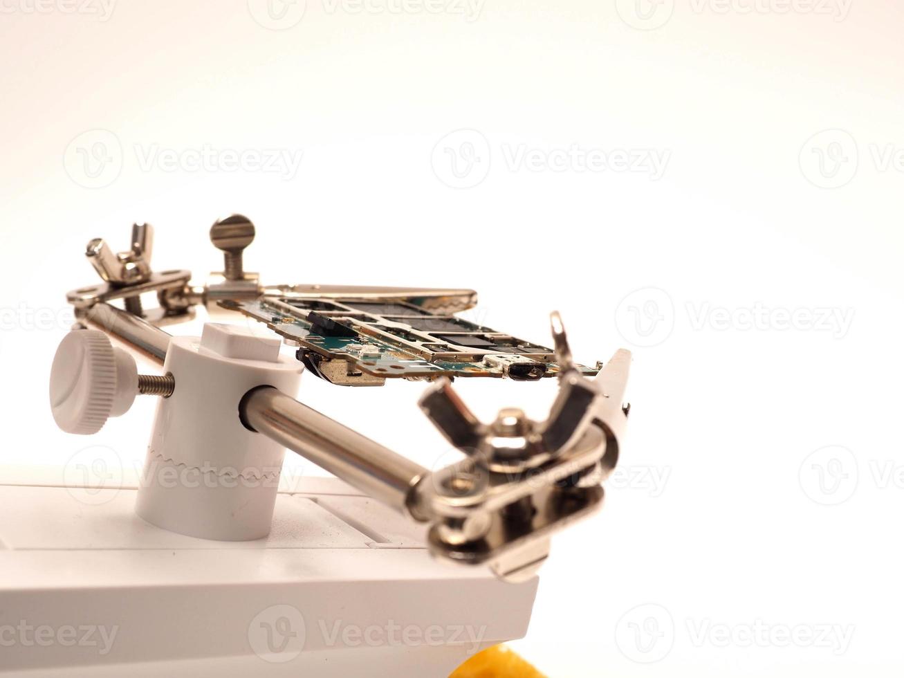 Close up shoot of printed circuit board PCB sitting on a white repair stand with magnifier for better examining small parts photo