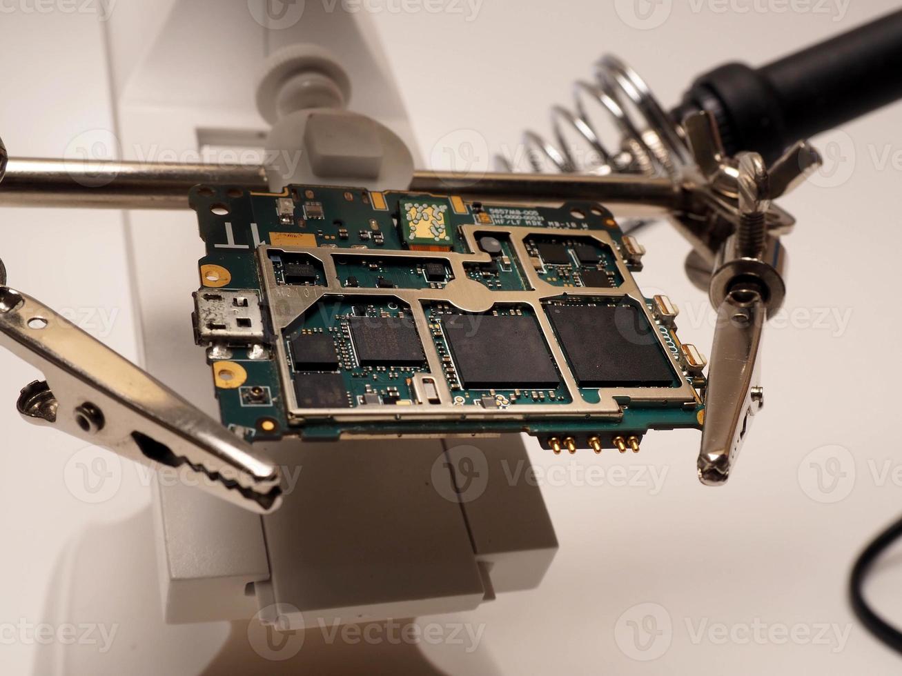 Close up shoot of printed circuit board PCB sitting on a white repair stand with magnifier for better examining small parts photo