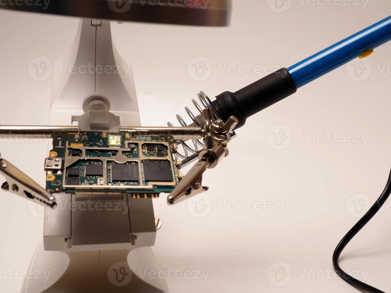 Close up shoot of printed circuit board PCB sitting on a white repair stand with magnifier for better examining small parts photo