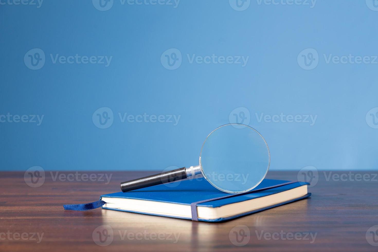 Not book with magnifying glass on wooden desk in information library of school or university, concept for education, reading , study, copy space and blue background. photo
