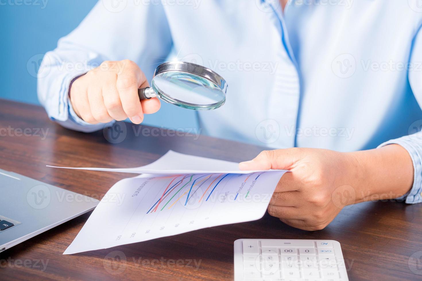 mano de mujer de negocios profesional sosteniendo y usando papel de documento de finanzas de búsqueda de lupa en el escritorio en la oficina, mujer de negocios mirando datos con análisis de estadísticas foto