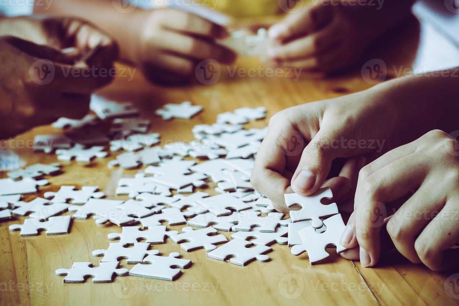 Hands of a person little child and parent playing jigsaw puzzle piece game together on wooden table at home, concept for leisure with family, play with children's development, education and fun. photo