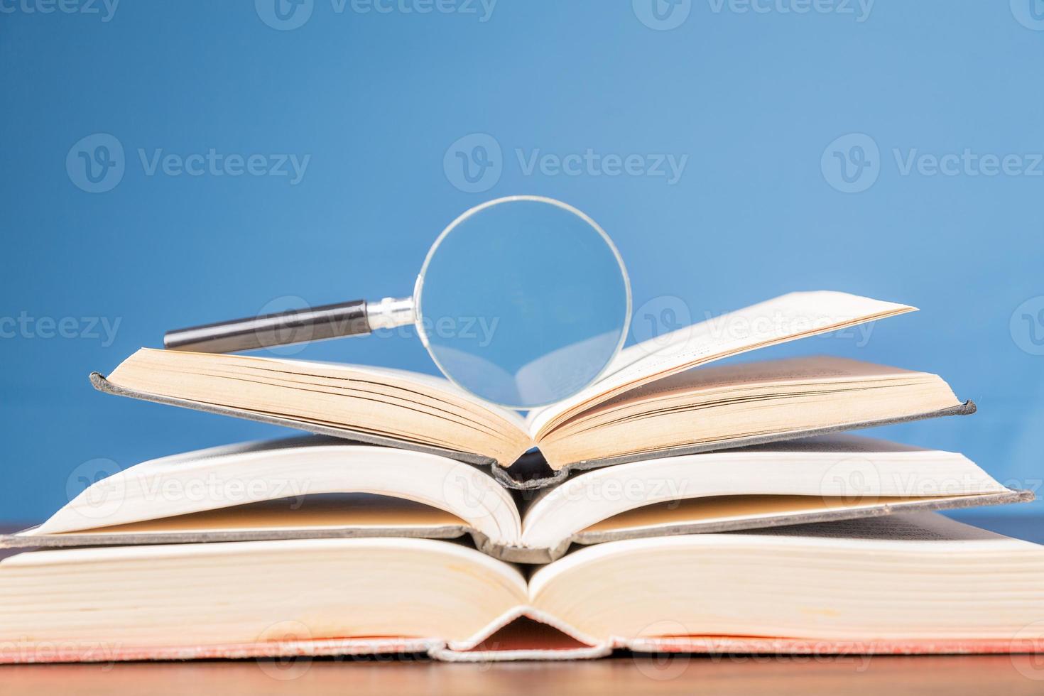 open book with magnifying glass on wooden desk in information library of school or university, concept for education,reading , study, copy space and blue background. photo