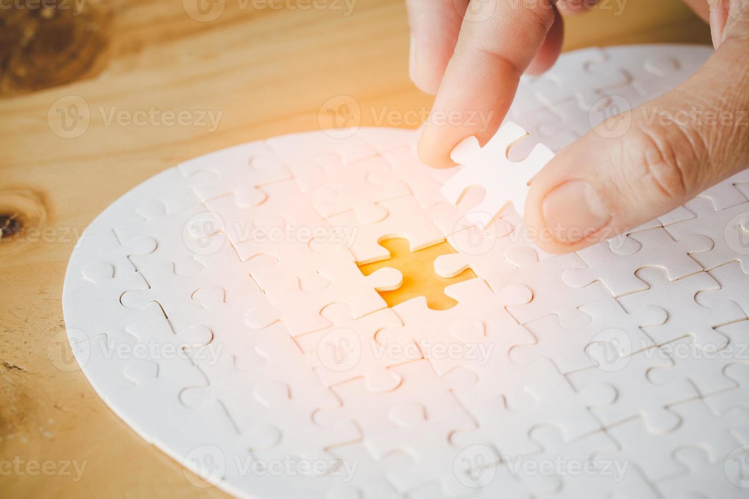 Close up hand holding and playing jigsaw game incomplete. White part of jigsaw puzzle pieces on table background. concepts of problem solving, business, teamwork. photo