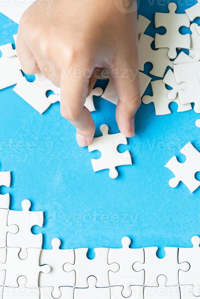 Close up hand holding and playing jigsaw game incomplete. White part of jigsaw puzzle pieces on blue background. concepts of problem solving, business, teamwork, Texture photo with copy space for text