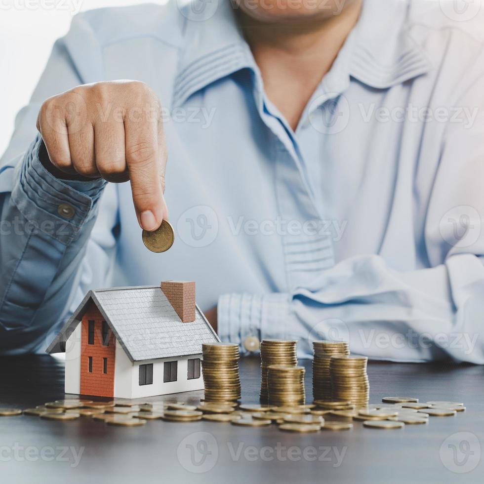 Hand putting coin in house model of coin for saving money for buying house. Savings plans for home, loan, investment, mortgage, finance and banking about house concept. photo