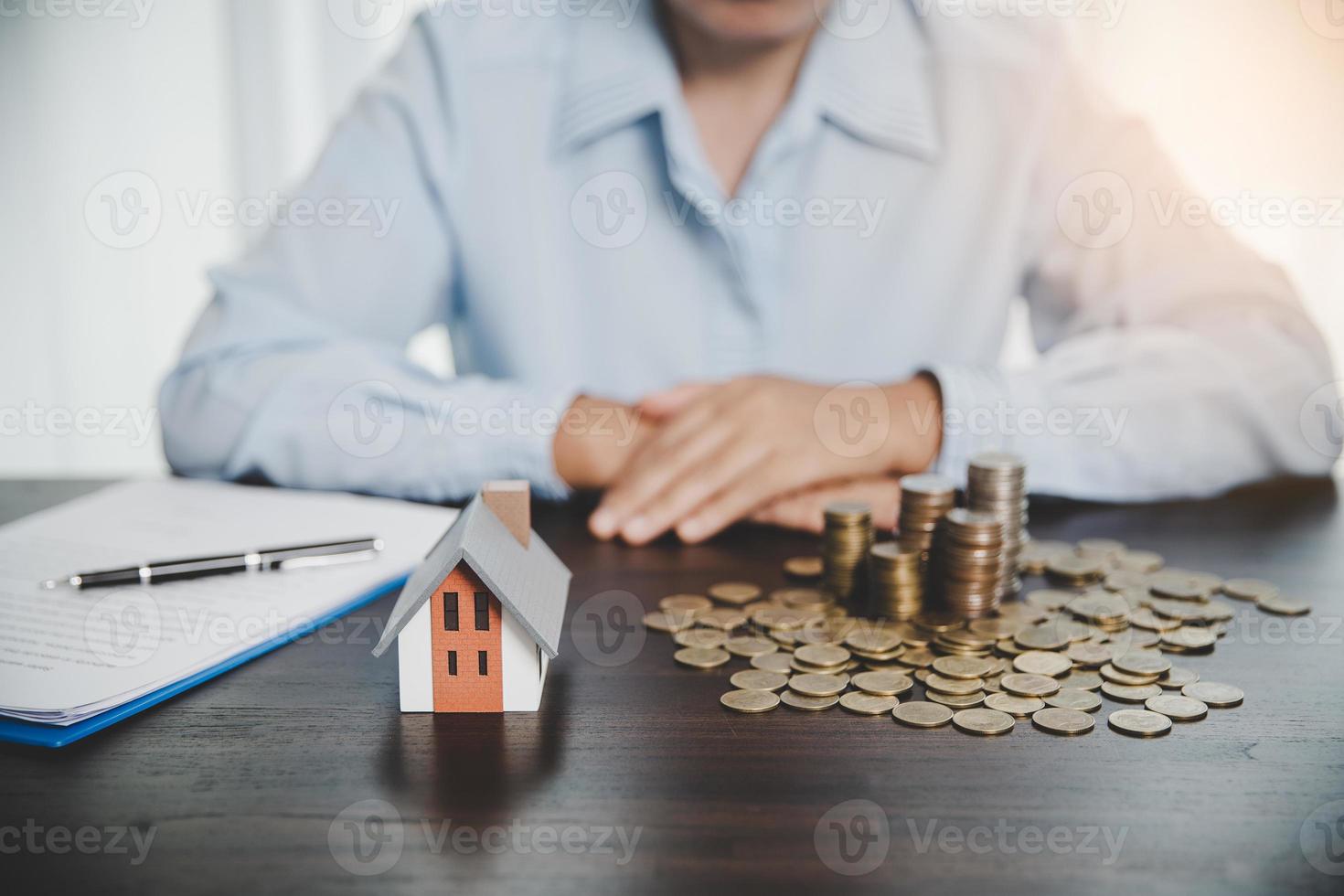 modelo de casa con monedas apiladas, la mano de negocios está planeando ahorrar dinero en monedas para comprar una casa. concepto de escalera de propiedad, hipoteca con inversión inmobiliaria y ahorro o inversión para una casa foto