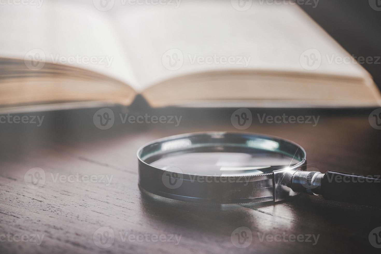 open book with magnifying glass on wooden desk in information library of school or university, concept for education,reading , study, copy space on table background. photo