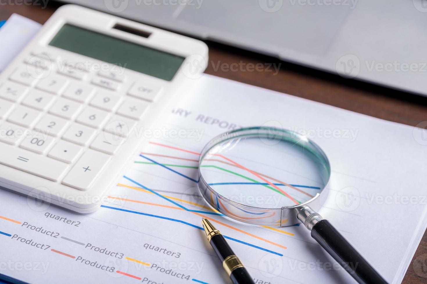 magnifying glass with business document financial paper chart statistic report on desk in office, closeup calculating machine with paperwork on table concept for analysis, market, banking photo
