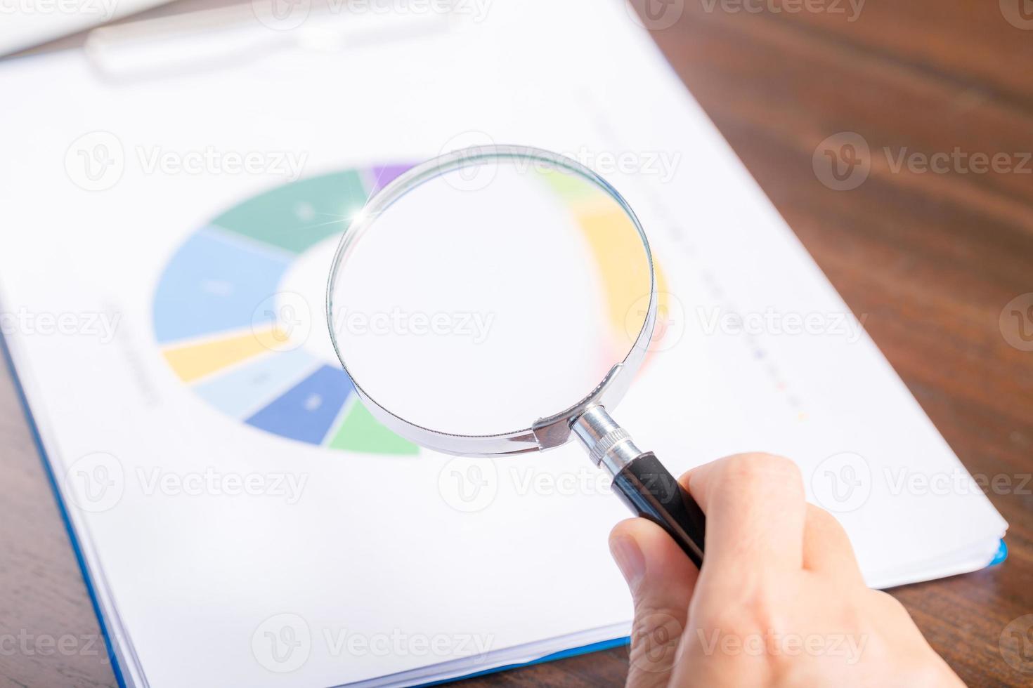mano de mujer de negocios profesional sosteniendo y usando papel de documento de finanzas de búsqueda de lupa en el escritorio en la oficina, mujer de negocios mirando datos con análisis de estadísticas foto
