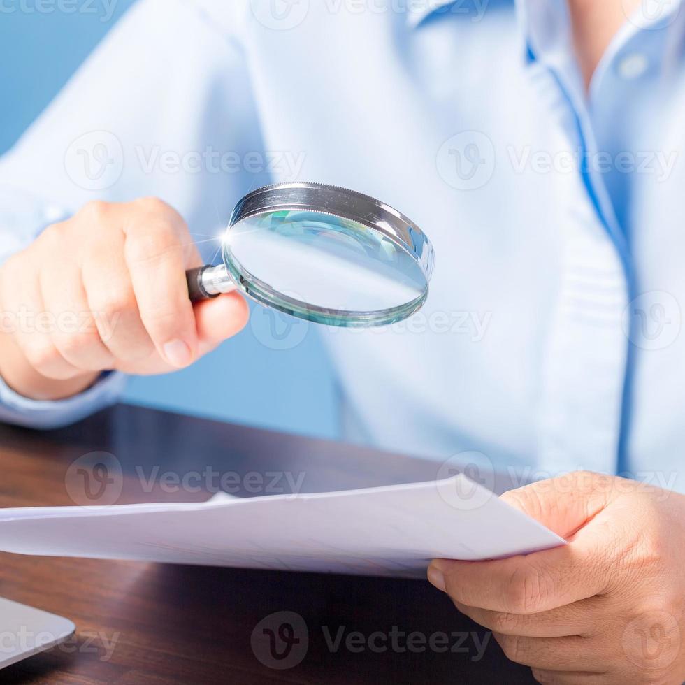 mano de mujer de negocios profesional sosteniendo y usando papel de documento de finanzas de búsqueda de lupa en el escritorio en la oficina, mujer de negocios mirando datos con análisis de estadísticas foto