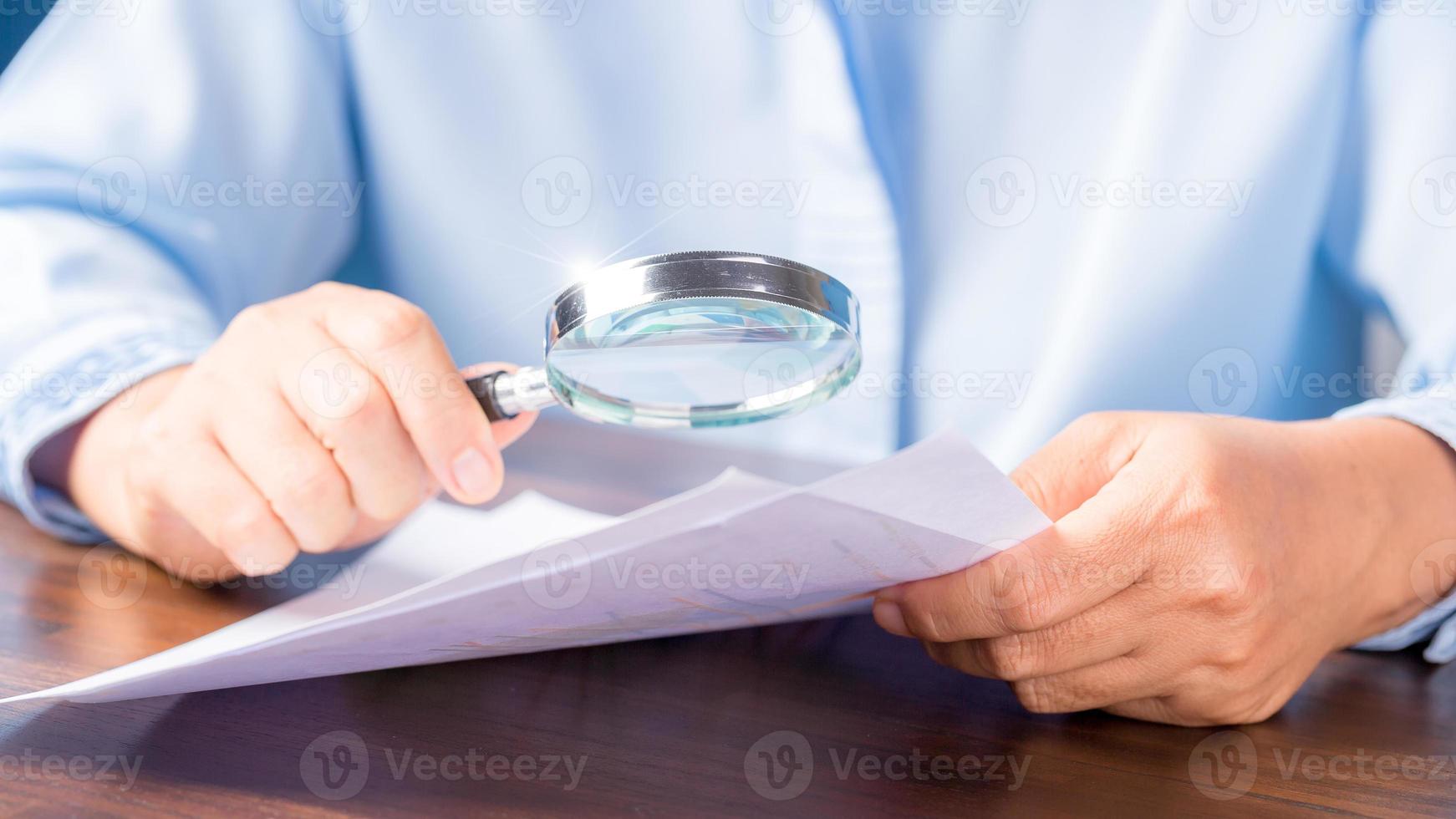 mano de mujer de negocios profesional sosteniendo y usando papel de documento de finanzas de búsqueda de lupa en el escritorio en la oficina, mujer de negocios mirando datos con análisis de estadísticas foto