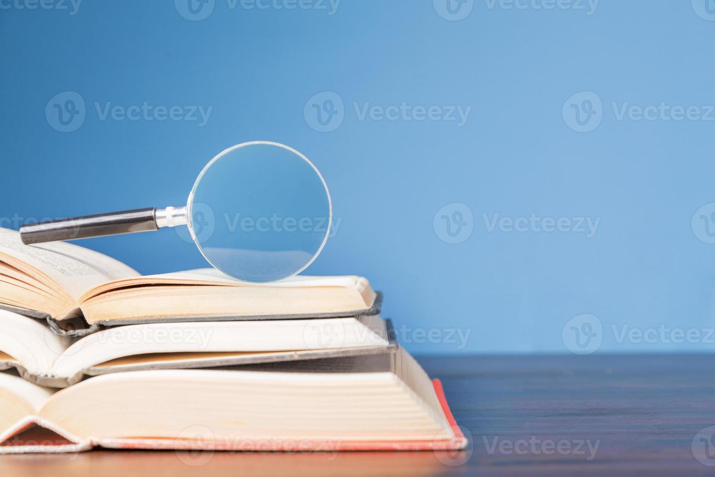 open book with magnifying glass on wooden desk in information library of school or university, concept for education,reading , study, copy space and blue background. photo