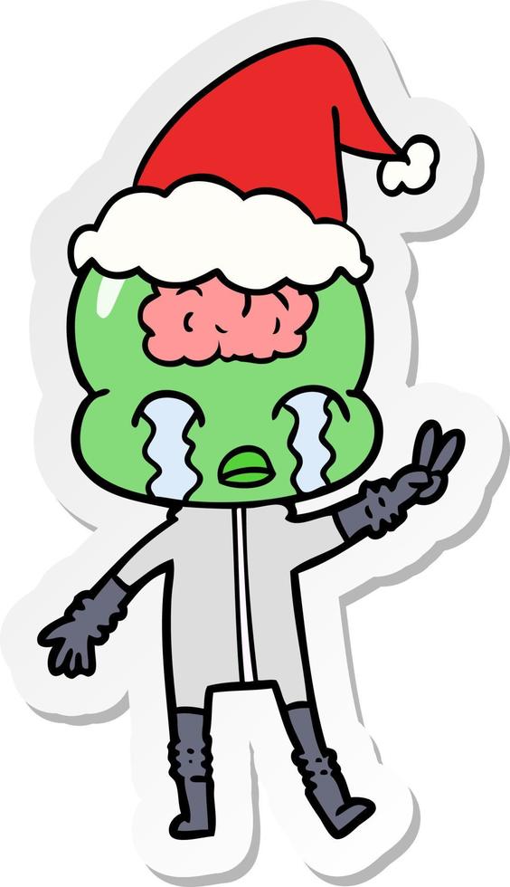 sticker cartoon of a big brain alien crying and giving peace sign wearing santa hat vector