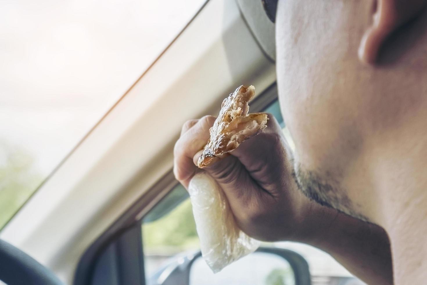 Man driving car while eating grilled  pork stick with sharp spike bamboo stick and sticky rice in plastic pack dangerously - multitasking driving bad behave danger risk drive concept photo