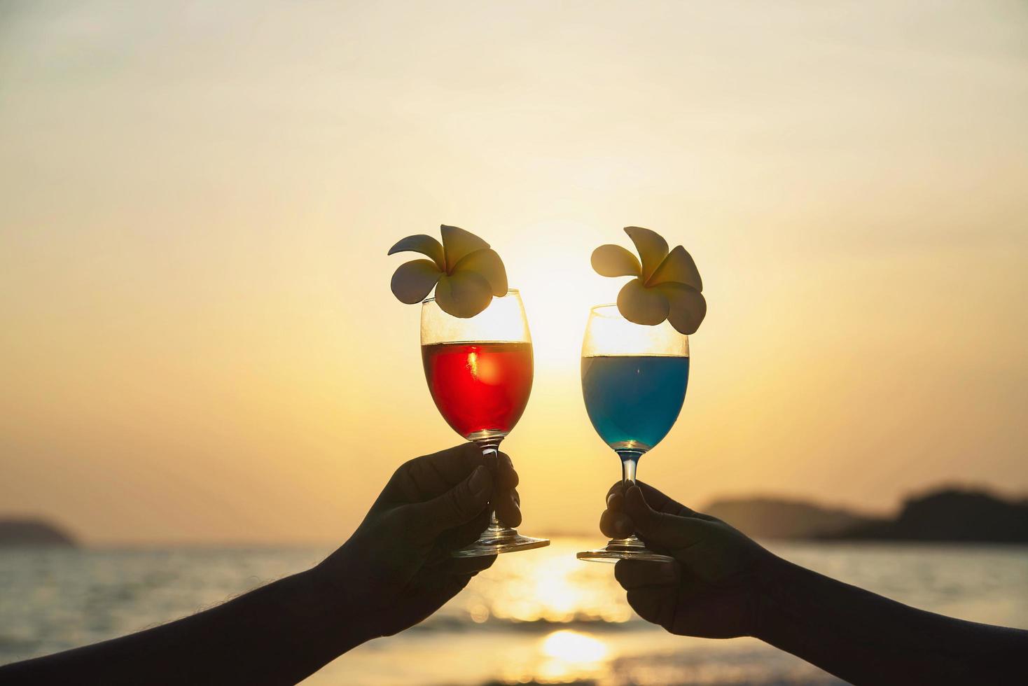 Silueta pareja mano sujetando la decoración de copas de cóctel con flor de plumeria con fondo de playa - feliz relax celebración vacaciones en concepto de naturaleza del mar foto