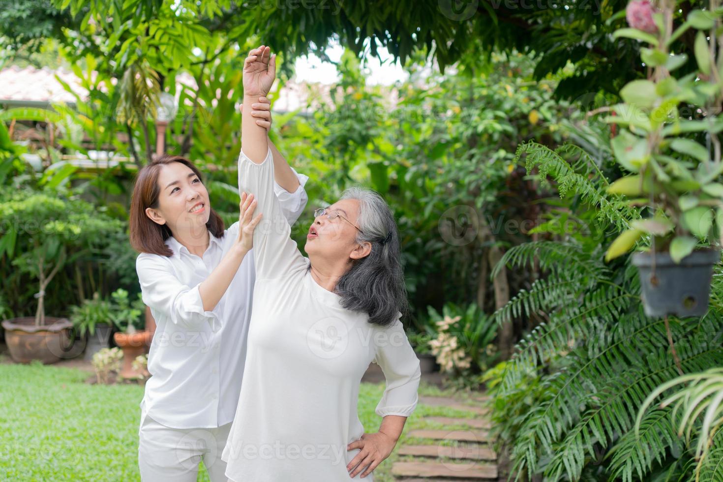 An old elderly Asian woman and exercise in the backyard with her daughter.  Concept of happy retirement With care from a caregiver and Savings and senior health insurance, Happy family photo