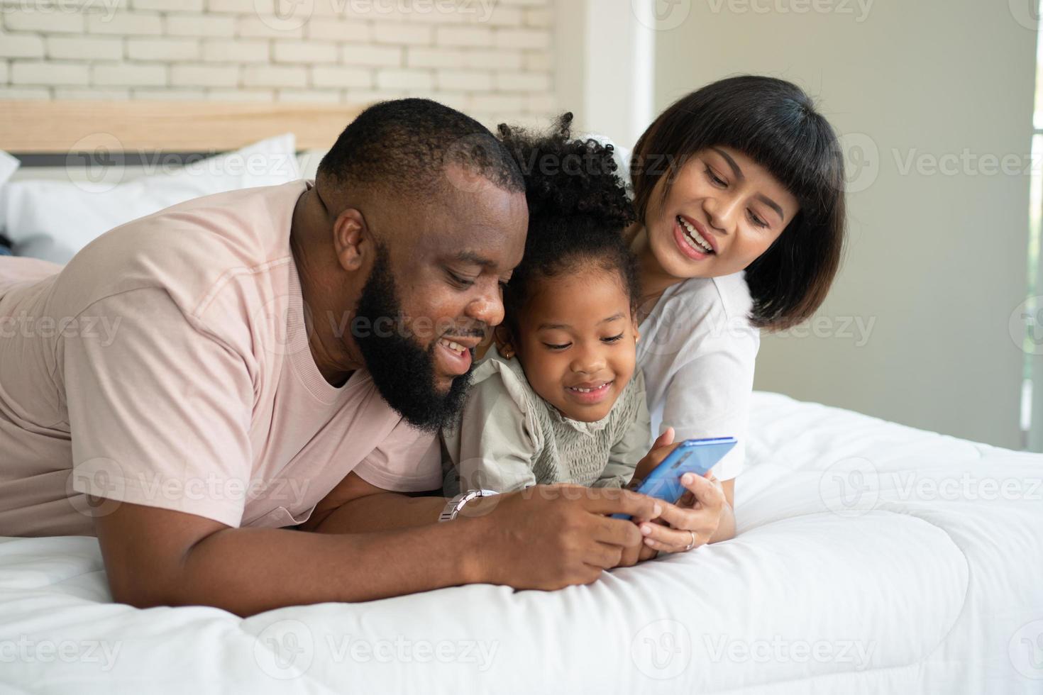 The family has fun and plays education games online with a smartphone at home in the bedroom. Concept of online education and caring from parents. photo