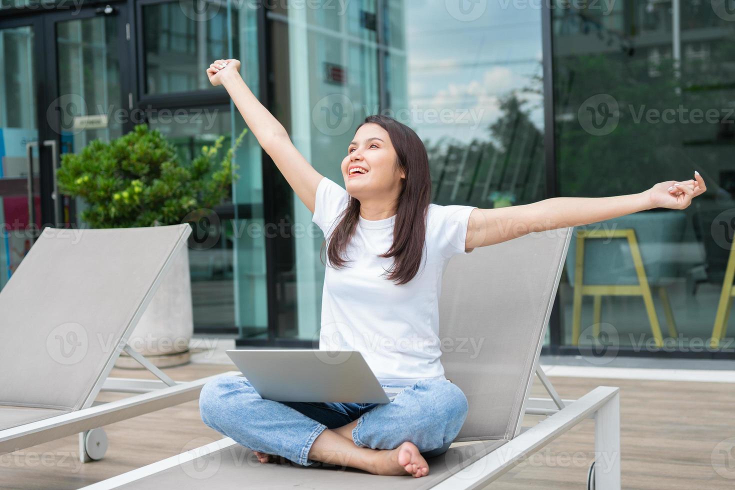 Happy young entrepreneur woman sitting on tanning bed beside pool and using laptop computer for remote online working digital, online business project in quiet yard of resort house, Work on vacation photo