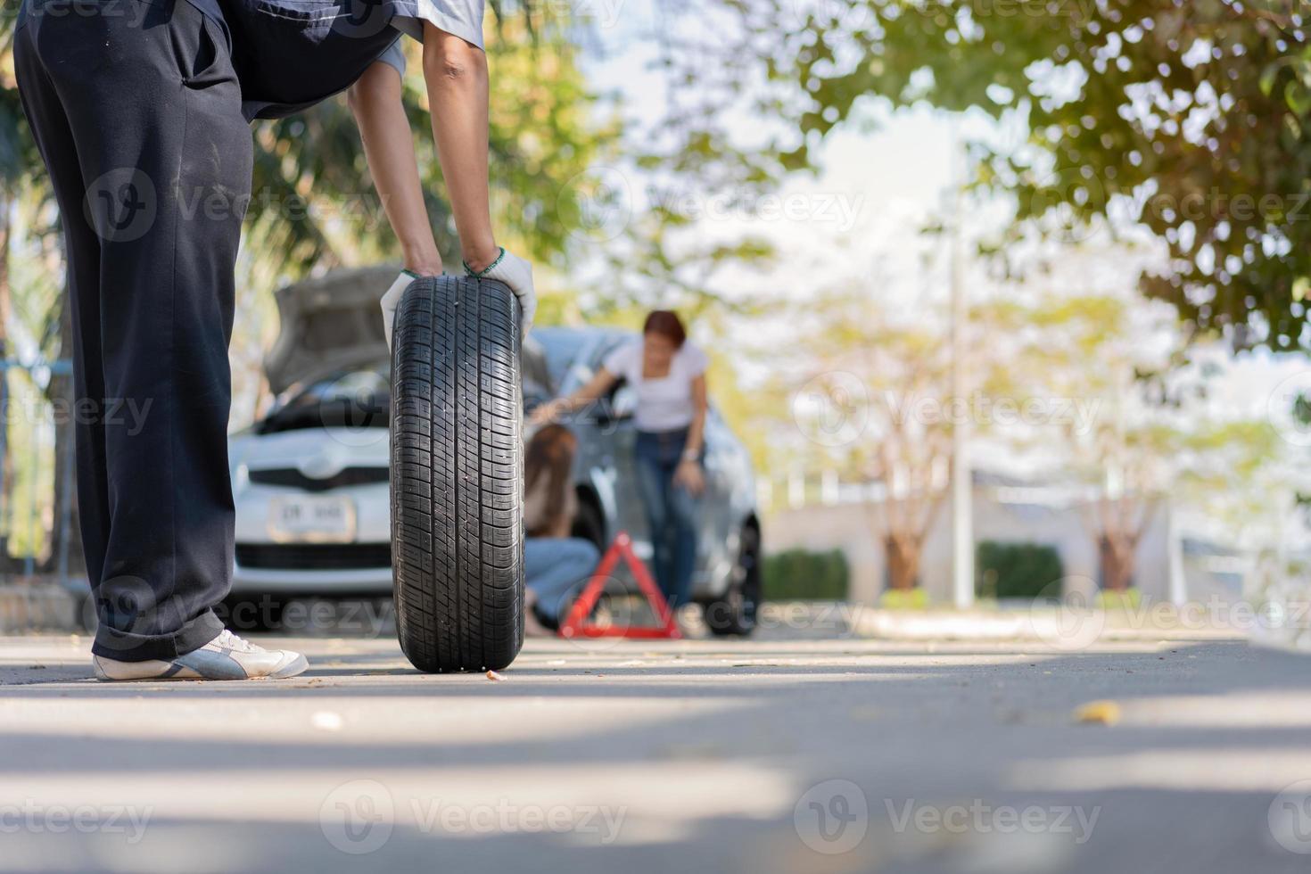 Expertise mechanic man in uniform holding a tire for help a woman for changing car wheel on the highway, car service, repair, maintenance concept. photo