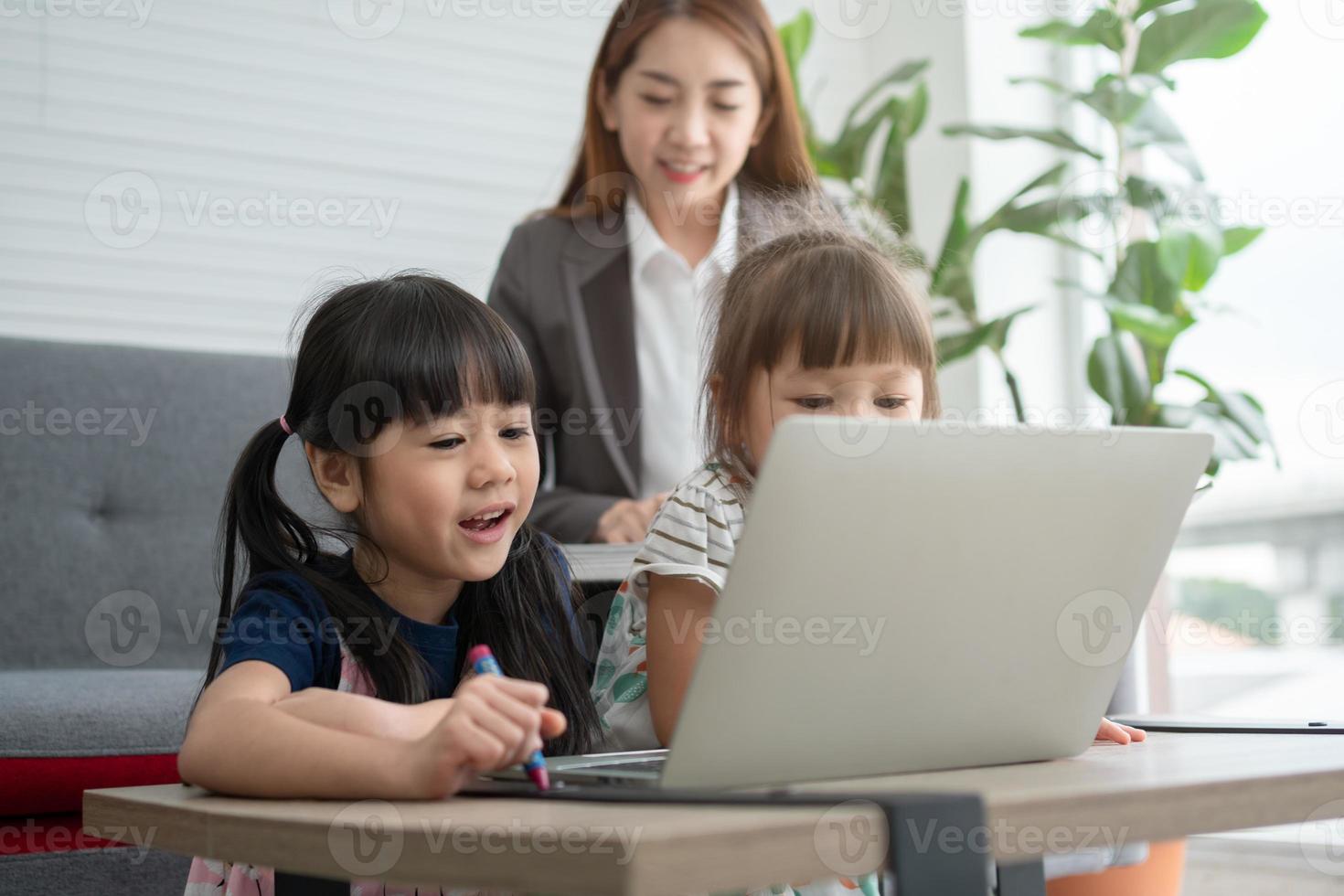 Asian mother with her two grandchildren having fun and playing education games online with a digital computer laptop at home in the living room. Concept of online education and caring from parents. photo