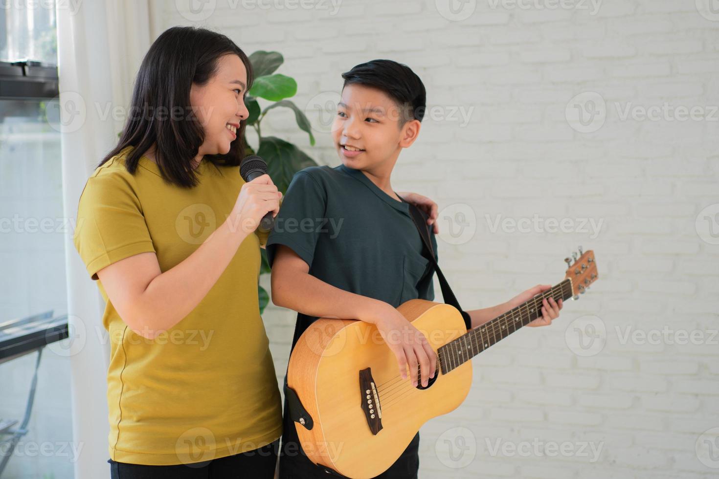 Asian boy playing guitar and mother sing a song and embrace, feel appreciated and encouraged. Concept of a happy family, learning and fun lifestyle, love family ties photo