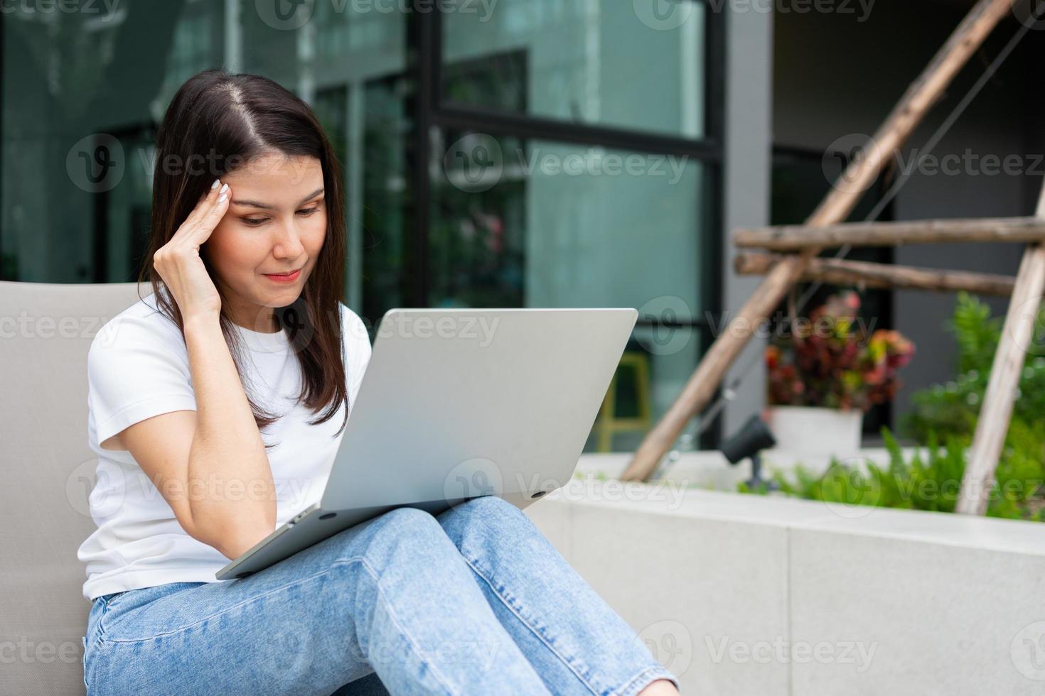 Happy young entrepreneur woman sitting on tanning bed beside pool and using laptop computer for remote online working digital, online business project in quiet yard of resort house, Work on vacation photo