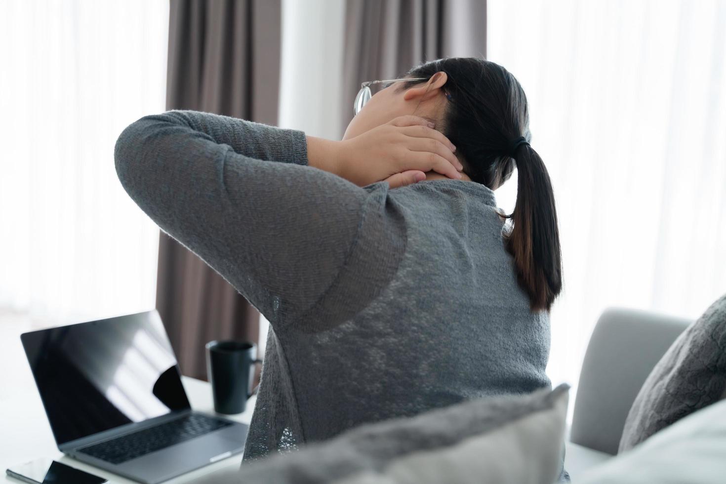 Tired stressed business woman suffering from fibromyalgia neck pain working at home sitting on sofa. Overworked young lady massaging neck feeling hurt pain from sedentary job photo