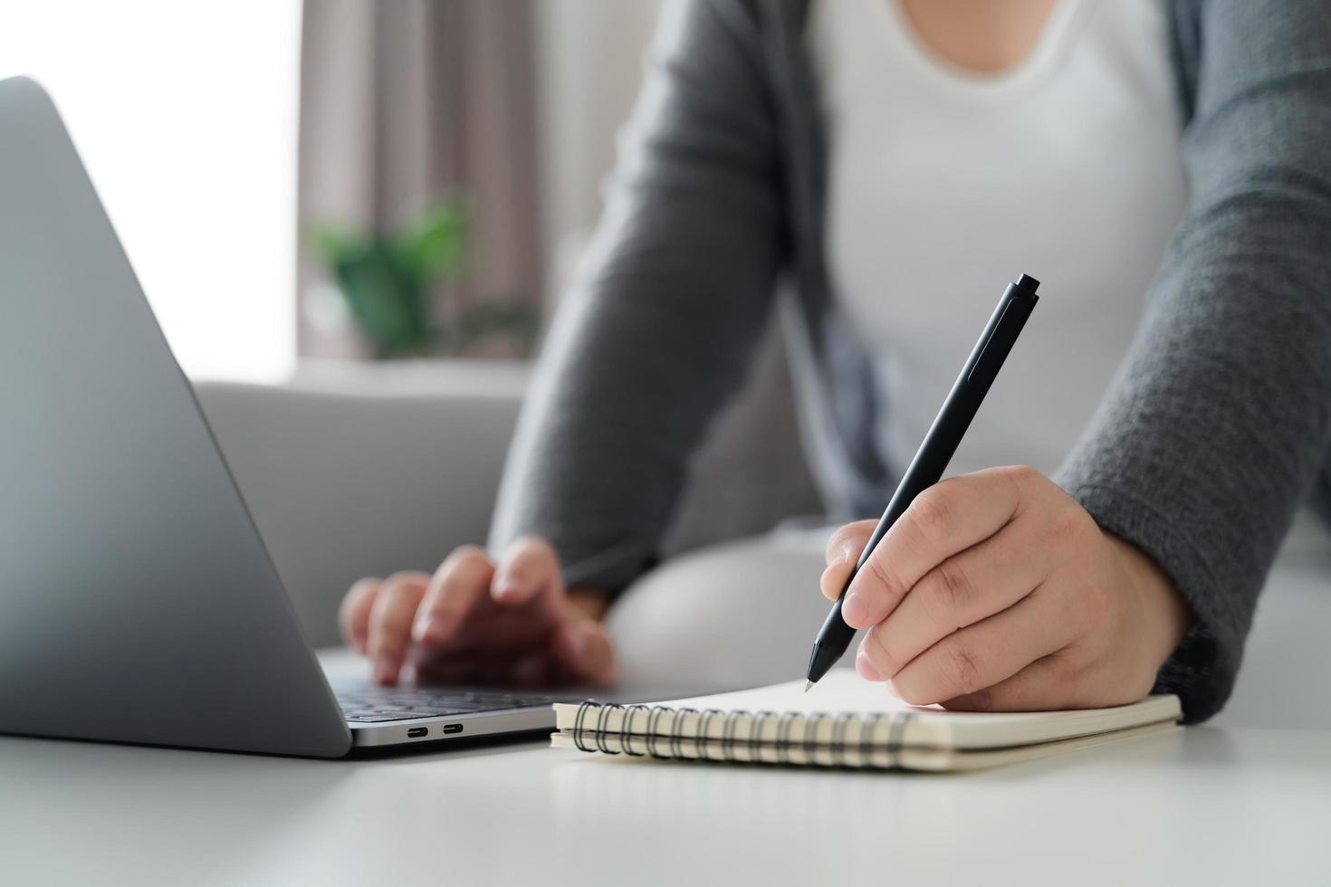 woman using laptop and writing on notepad with a pen working at home office or workplace. photo