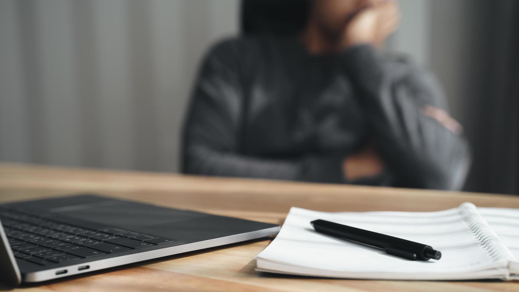 Tired businessman working on laptop with notepad and pen, resting head on hand, doing work overtime, stressed and bored photo